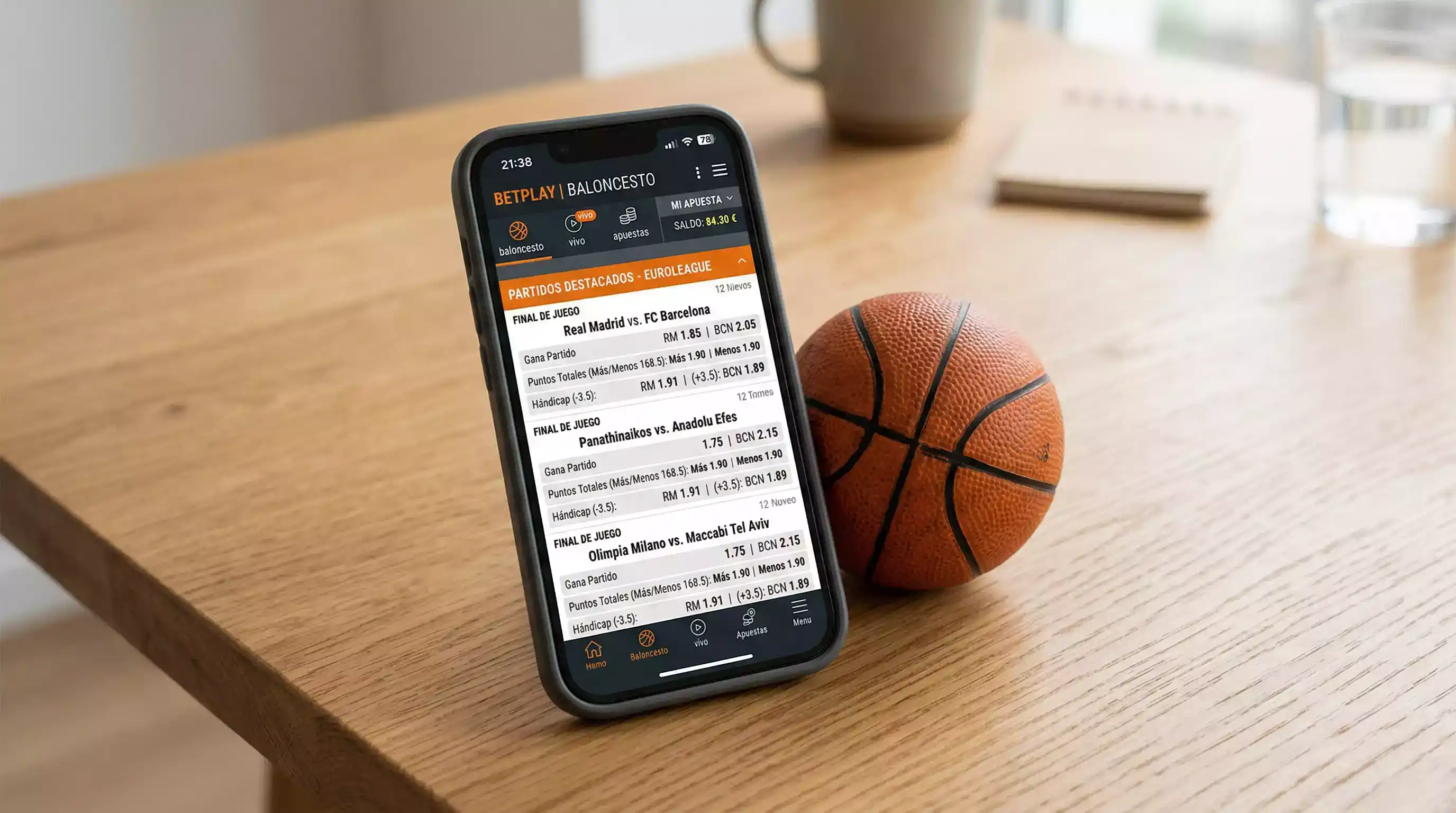 Teléfono móvil con aplicación de apuestas de baloncesto abierta sobre una mesa junto a un balón